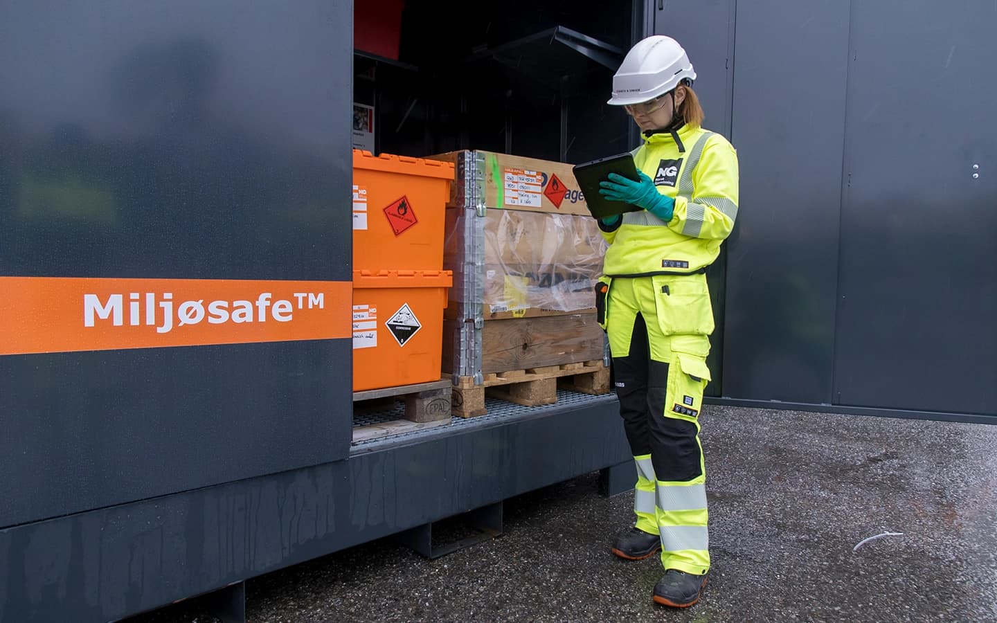Miljøsafe: container/skap med farlig avfall. Dame med gule arbeidsklær står foran. Foto.
